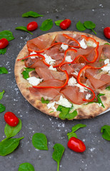 Colourful Italian pizza with prosciutto ham, pepper and decorated with tomato and basil