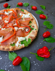 Colourful Italian pizza with prosciutto ham, pepper and decorated with tomato and basil