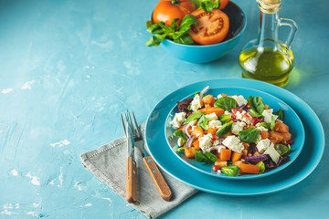Blue plate of fresh superfoods healthy salad with red onion, tomatoes, doucette (lambs lettuce, corn salad, field salad) and feta cheese. Light blue surface.