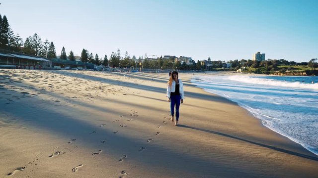 Panning shot of young attractive woman walking along the sand at Coogee Beach, Sydney. 