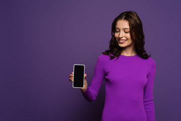 smiling girl showing smartphone with blank screen on purple background