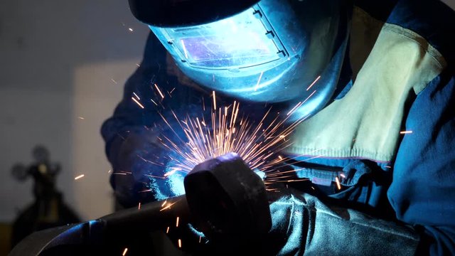 Electrode works of crafts man in protective wear using welding machine on factory line of heavy industry. Process of drilling iron parts. Bright sparks of heat manufacture on laborer workshop closeup