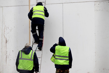 Fototapeta premium Workers near the wall of a building under construction. Man in uniform climbs the ladder