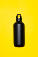 Close-up of black reusable aluminum thermo water bottle on yellow background.