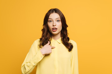 surprised girl pointing with finger at herself while looking at camera  isolated on yellow
