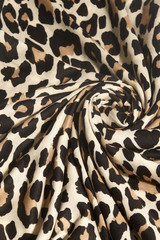 Macro shot of a beige fabric with black and brown leopard print. The cloth folds are lined as a flower-form figure.  
