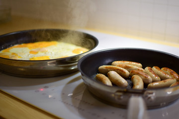 Cooking on an induction cooker. Fried eggs and sausages in pans.