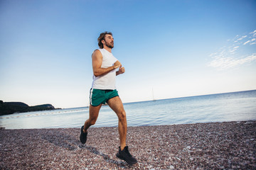 Running man jogging on beach. Male runner training outside working out.