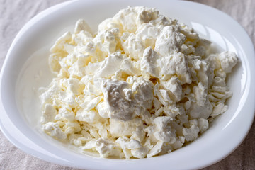 A white plate filled with cottage cheese on a linen tablecloth. Closeup view. Selective focus