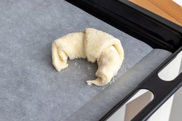 Croissant prepared for baking from a cottage cheese dough sprinkled with sugar on a parchment paper on a baking sheet. Sweet bagel before loading into the oven. Process of making curd bagels