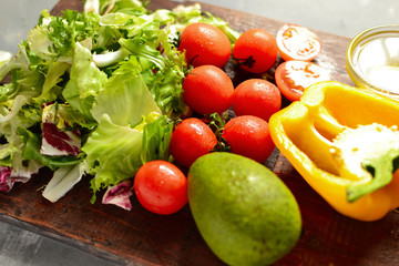 Ingredients for vegan spring and summer salad. Vegetables on a cutting board. Tomatoes, sweet yellow pepper, lettuce, dressing, avocado, oil in a bowl.