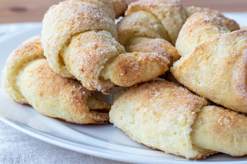 Sugar-frosted croissants from a cottage cheese dough on a white plate on a gray linen tablecloth just taken out of the oven. Tea snack for breakfast. The process of making curd bagels or croissants