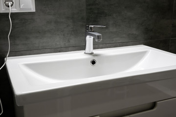 Fototapeta premium Modern white rectangular sink with chromed metal faucet for hot and cold water in a stylish bathroom with gray concrete wall. Selective focus