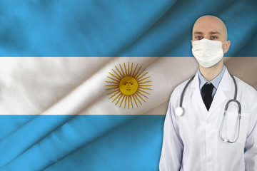 doctor in white uniform with a stethoscope against the background of the silk national flag of...