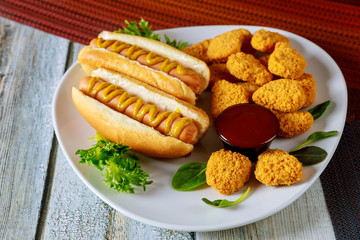 Baked crispy chicken nuggets and hot dogs on white plate.