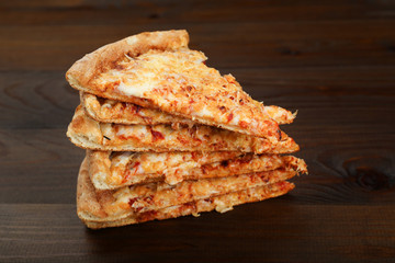 stack of pieces of cheese pizza on dark wooden background