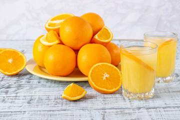 Glass of orange juice with ice cubes on a wooden table and a plate with oranges.