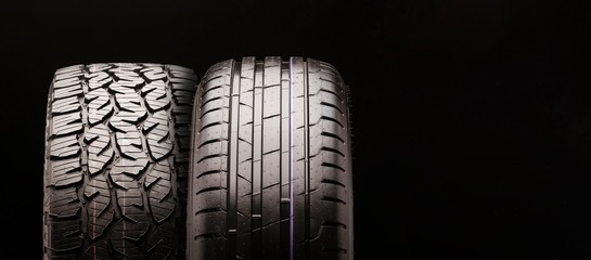 a mud tire for pickups and trucks and a passenger tire side by side together, for summer. Two wheels close- up , long elongated concept layout copy space on a black background - obrazy, fototapety, plakaty