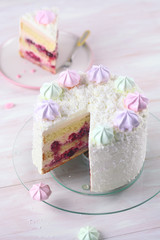 Cherry Layer Cake decorated with fine coconut flakes and colored meringue cookies, on white wooden background.