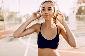 Attractive athletic young woman, in sportswear, standing outdoors and listening to music with headphones
