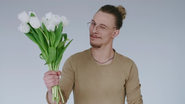 Young handsome man, lovelace flirts, gives flower bouquet, winks and looks at camera