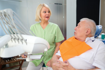 Surprised dentist woman talking with senior man patient in dental clinic. Dental care for older people. Dentistry, medicine and health care concept