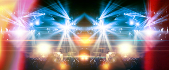 Colourful concert crowd in front of a lit stage inside a concert venue, during a music festival