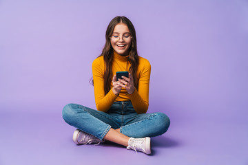 Image of young woman holding smartphone while sitting with legs crossed