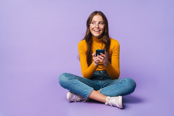 Image of young woman holding smartphone while sitting with legs crossed