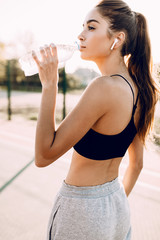 Sporty young girl, in top and sweatpants, drinking water from a bottle