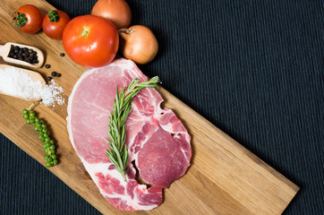 Top view raw pork chop meat on wood plate with vegetables, spices, salt and black pepper in dark black cloth table