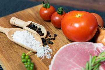 Raw pork chop meat on wood plate with vegetables, spices, salt and black pepper in dark black cloth table. Focus on ingredient