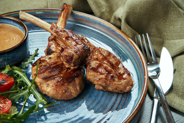A grilled rack of young calf or lamb (beef) with peanut sauce and cherry tomatoes in a blue plate on a wooden background. Selective focus, close up