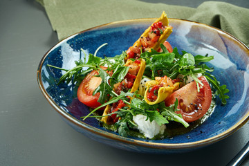 Close up view on Appetizing Italian caprese salad with fresh tomatoes, soft mozzarella, arugula and sauce in blue bowl rustic background. Selective focus, close up