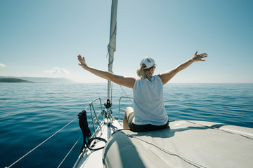 Woman sitting on the ships bow enjoying the yacht trip with arms wide open. Sailing, yachting and travel concept.