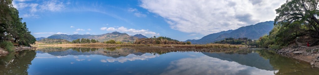 The country river reflects the mountains and trees in the distance