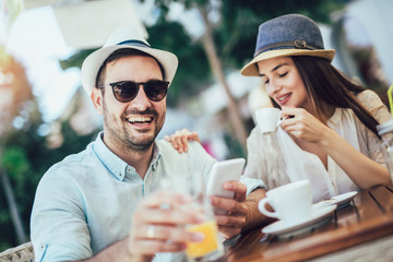 Beautiful loving couple sitting in a cafe enjoying in coffee and using phone