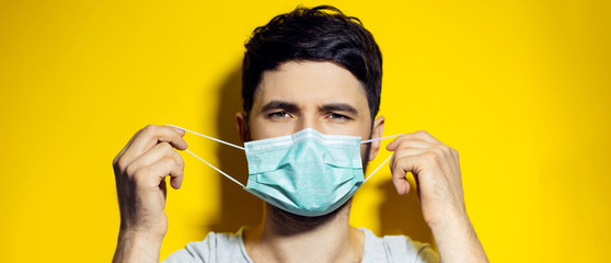 Close-up portrait of young man, takes off the medical protective flu mask, on background of yellow...