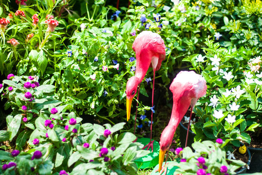 Artificial plaster-made pink flamingo standing in the center of colorful flowers