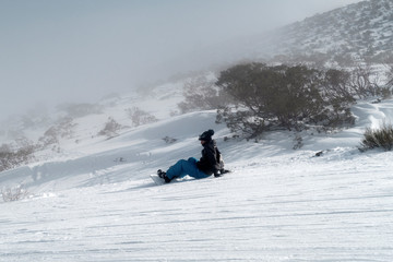 Snowboarder sitting facing foggy hill.