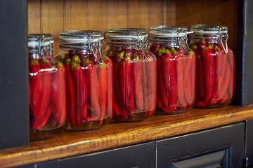 Fototapeta na wymiar Preserved vegetables in glass jars on a wooden shelf of a cabinet. Pickled hot chili peppers.