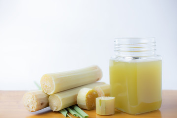 Fresh squeezed sugar cane juice in clear glass with cut pieces cane on white background.