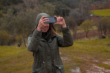 Young blonde girl in forest taking a picture with smartphone