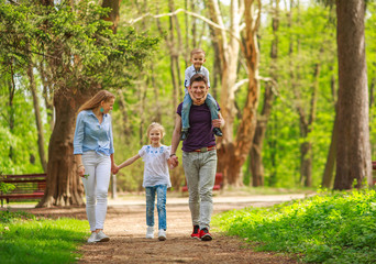 Naklejka na ściany i meble Happy young family parents with child in green summer city park have fun walking together
