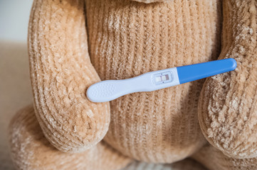 Teddy bear and positive pregnancy test close up and copy space. Children's toy bear, booties, test.