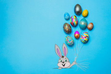 Smiling cartoon Bunny holds painted Easter eggs in shape of balloons by the strings. Happy Easter concept. Bright blue background, top view, copy space, banner