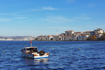 Fototapeta na wymiar Picturesque panoramic view of Degirmendere (Kocaeli, Turkey) at sunny winter day. Bright blue water and small fishing boat in the foreground