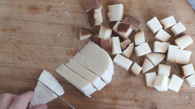 Directly above footage of woman cutting, preparing Circassian cheese on the cutting board.
