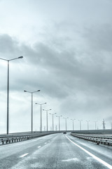 a road with white markings on the asphalt against a gray sky. Road fence