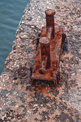 Rusty steel double berth on a fragment of an old concrete pier against a background of turquoise sea water